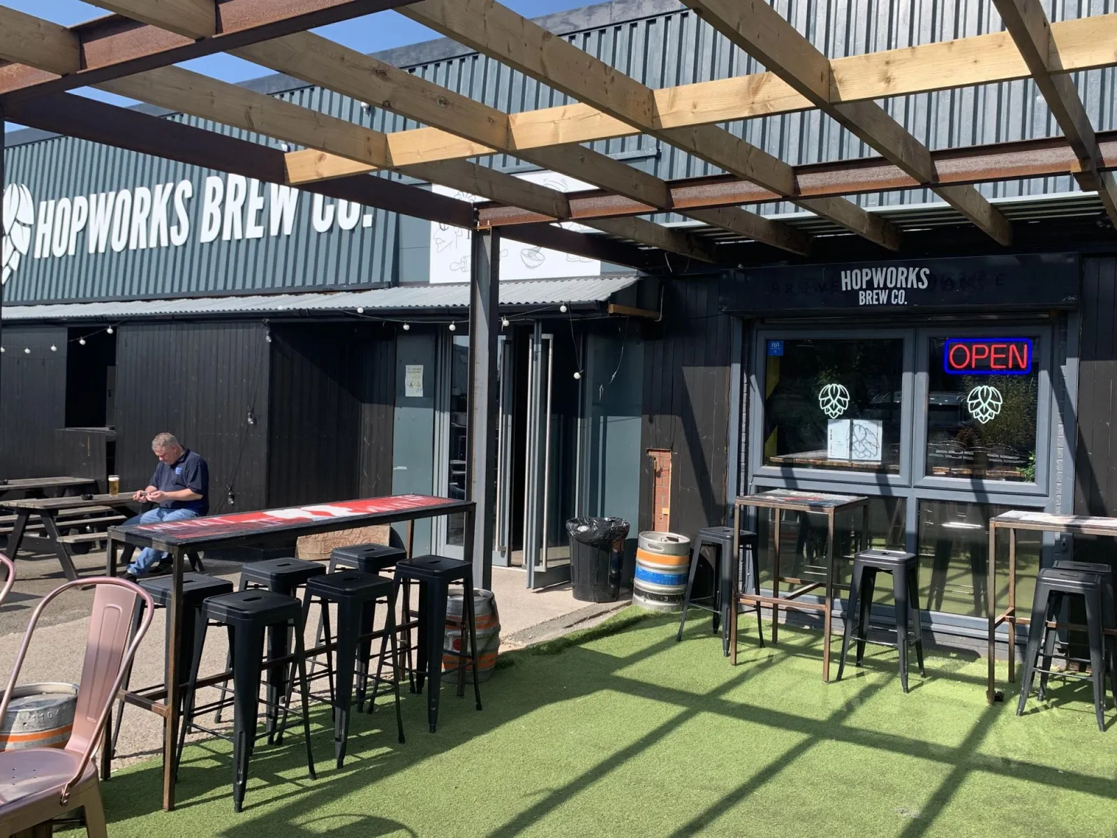 Outdoor seating area beside the taproom entrance, with a neon 'OPEN' sign in the window