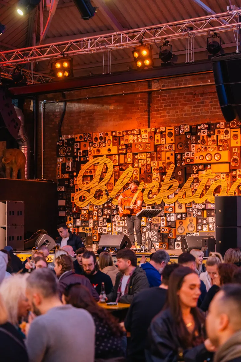The market at night, a large Blackstock sign in warm light above the trading units with a busy crowd at the tables below.
